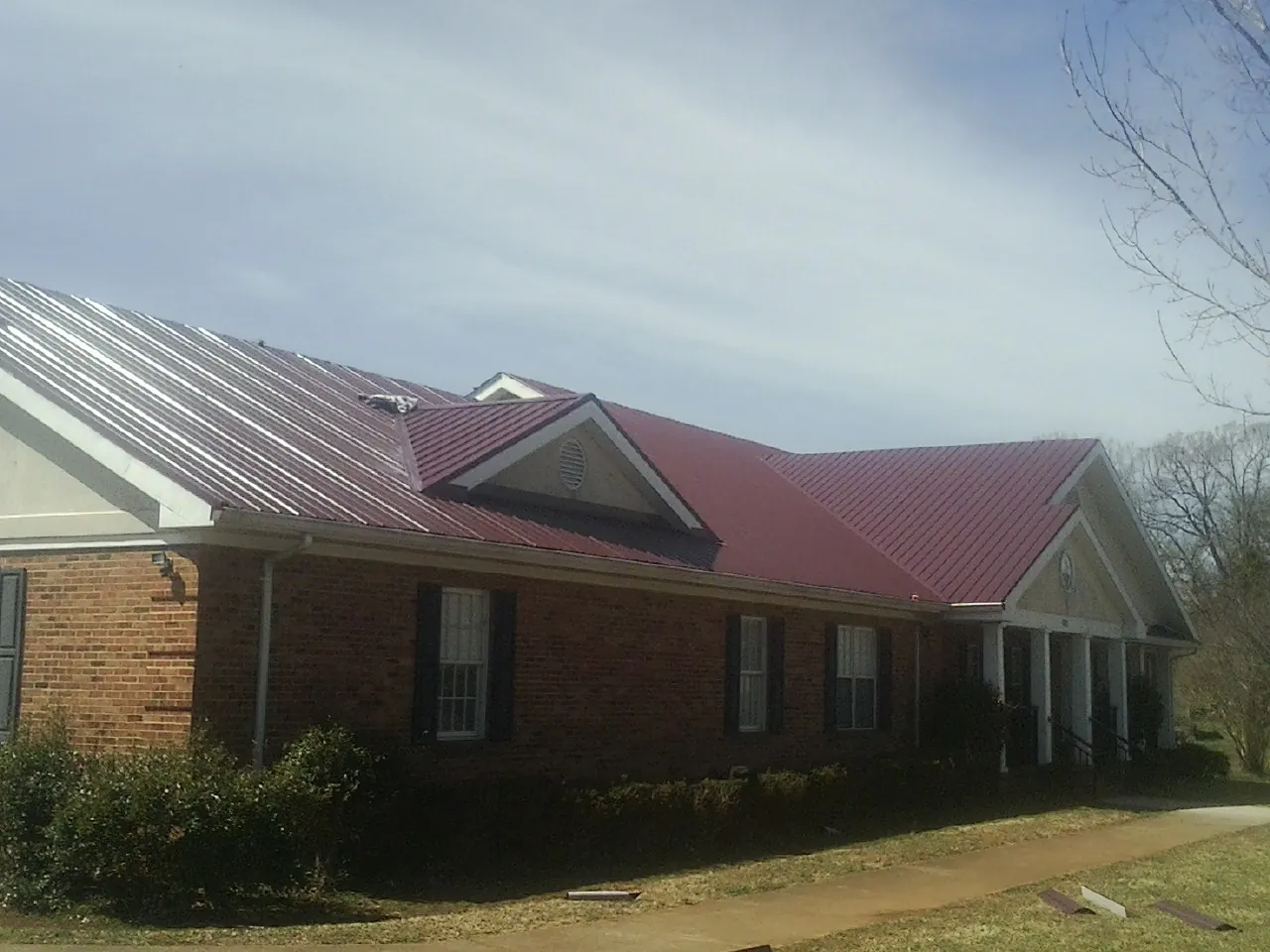 Red metal roof with gabled entries on a long brick building, from a Hail Damage Roof Repair job in Cleveland